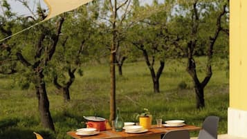 Un tavolo da pranzo all'aperto con sedie, una parete gialla e un prato con alberi sullo sfondo.