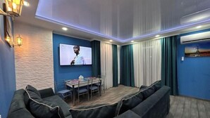 Un salon moderne avec un canapé aux lignes courbes, une table à manger et un téléviseur à écran plat fixé au mur.