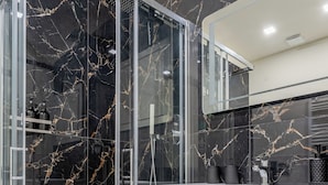 Un baño moderno con ducha envuelta en cristal, paredes de mármol y un tocador blanco.