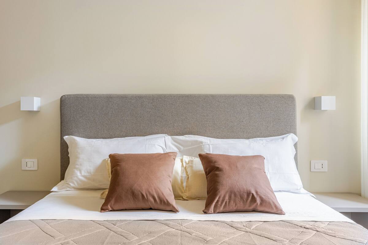 A neatly made bed with a grey headboard, white and brown pillows, and a beige quilt.