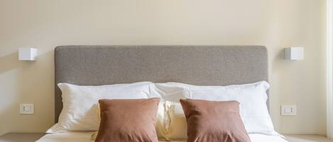 A neatly made bed with a grey headboard, white and brown pillows, and a beige quilt.