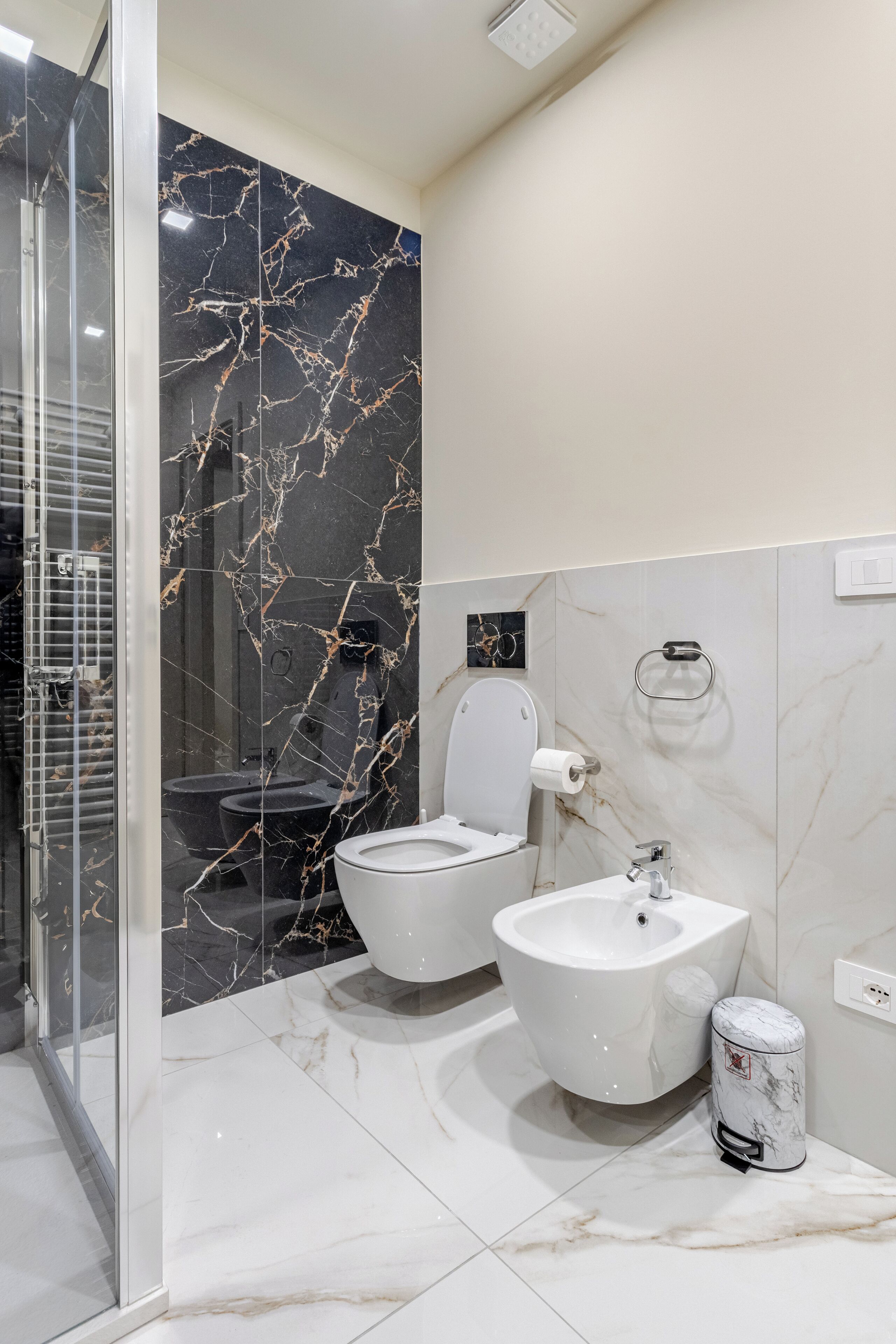 A modern bathroom with a glass shower enclosure, a toilet, a bidet, and a sink.