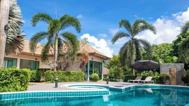 A swimming pool with tiled edges, surrounded by palm trees and a building with a thatched roof. - Naya Poly Pool Villa-80 (Phuket)