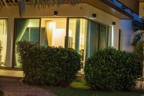 Un hotel con entrada de vidrio, césped bien cuidado y un área de estar exterior visible.
