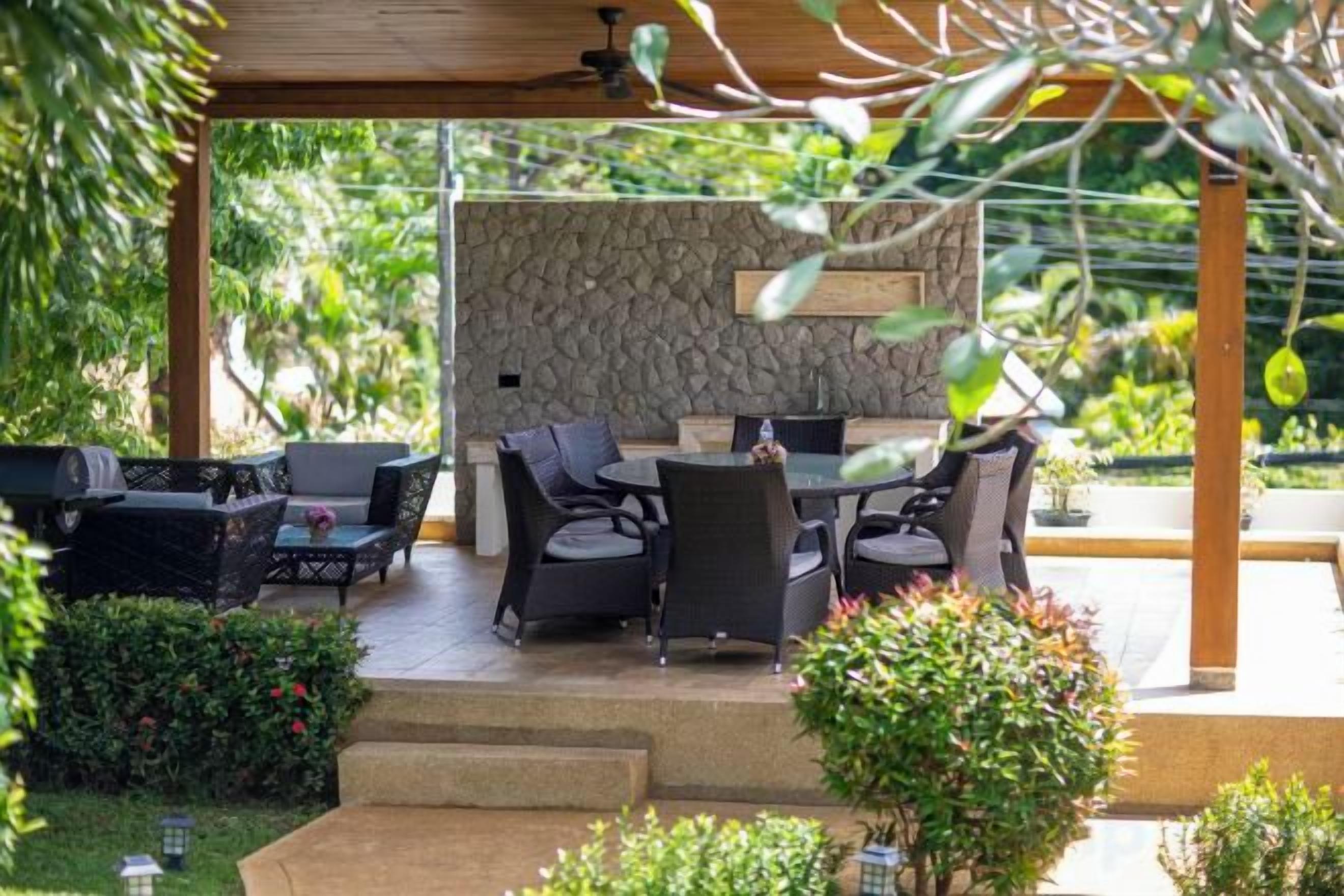 Um pátio externo com parede de pedra, móveis de jardim e uma pérgula.