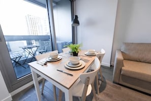 A dining area with a table set for four, a potted plant, and a sofa in the background. - A Chic 2BR, CBD Apartment Near Southern Cross (Melbourne)