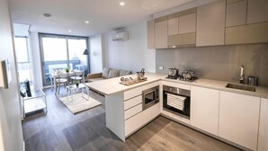 A modern kitchen with a central island, built-in oven, and a dining area with a table and chairs. - A Chic 2BR, CBD Apartment Near Southern Cross (Melbourne)
