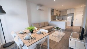 A modern living room with a dining table, white chairs, a sofa, and a kitchen area in the background. - A Chic 2BR, CBD Apartment Near Southern Cross (Melbourne)