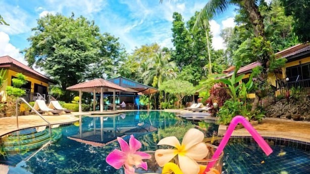 A pool area with a glass of tropical drink, surrounded by lush greenery and a small pavilion. - patong beautiful pool villa (Phuket)