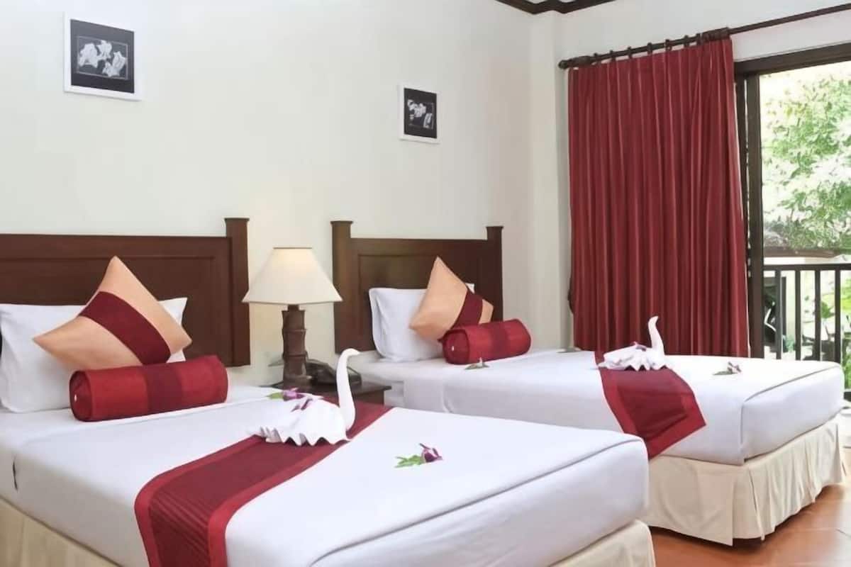 A hotel room with two beds, each with a swan decoration, red pillows, and a red throw blanket.