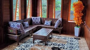 A wooden interior with a sofa, a table, and a window with a view of greenery. - Villa Zoya 1 (Megamendung)