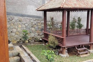 Un quiosco de madera con techo de tejas, rodeado por un muro de piedra y pequeñas plantas.