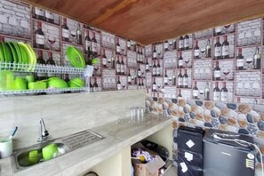A kitchen with a stone backsplash, a sink, and a shelf with green plates. - Villa Zoya 1 (Megamendung)