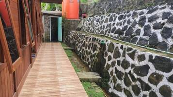 Un sendero de madera conduce a un muro de piedra con un diseño único, una puerta de madera y un depósito anaranjado grande.