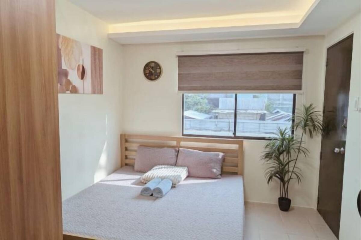 A bedroom with a bed, a clock, a window with a view, and a potted plant.