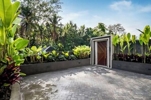 A paved courtyard with a wooden door, surrounded by lush tropical plants. - Villa Three Little Birds by BaliSuperHost (Bali)