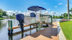 A boat docked at a wooden pier with a covered seating area, surrounded by water and greenery.