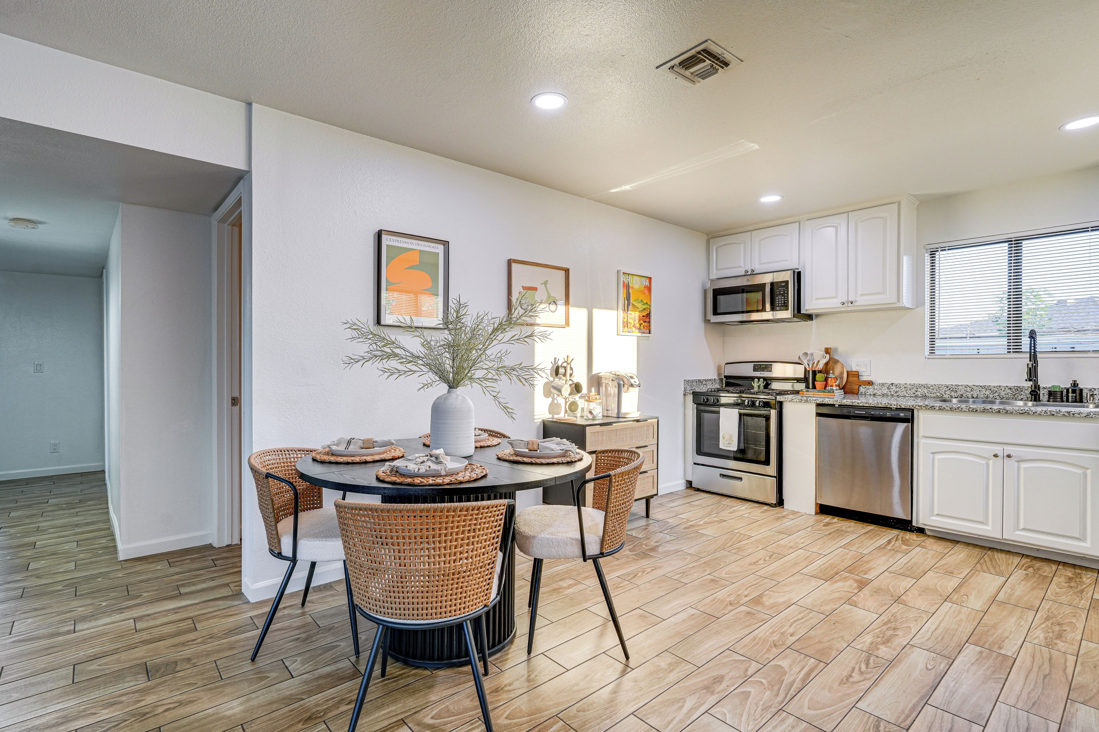 A modern kitchen with white cabinets, stainless steel appliances, and a dining area with wicker chairs and a round table.