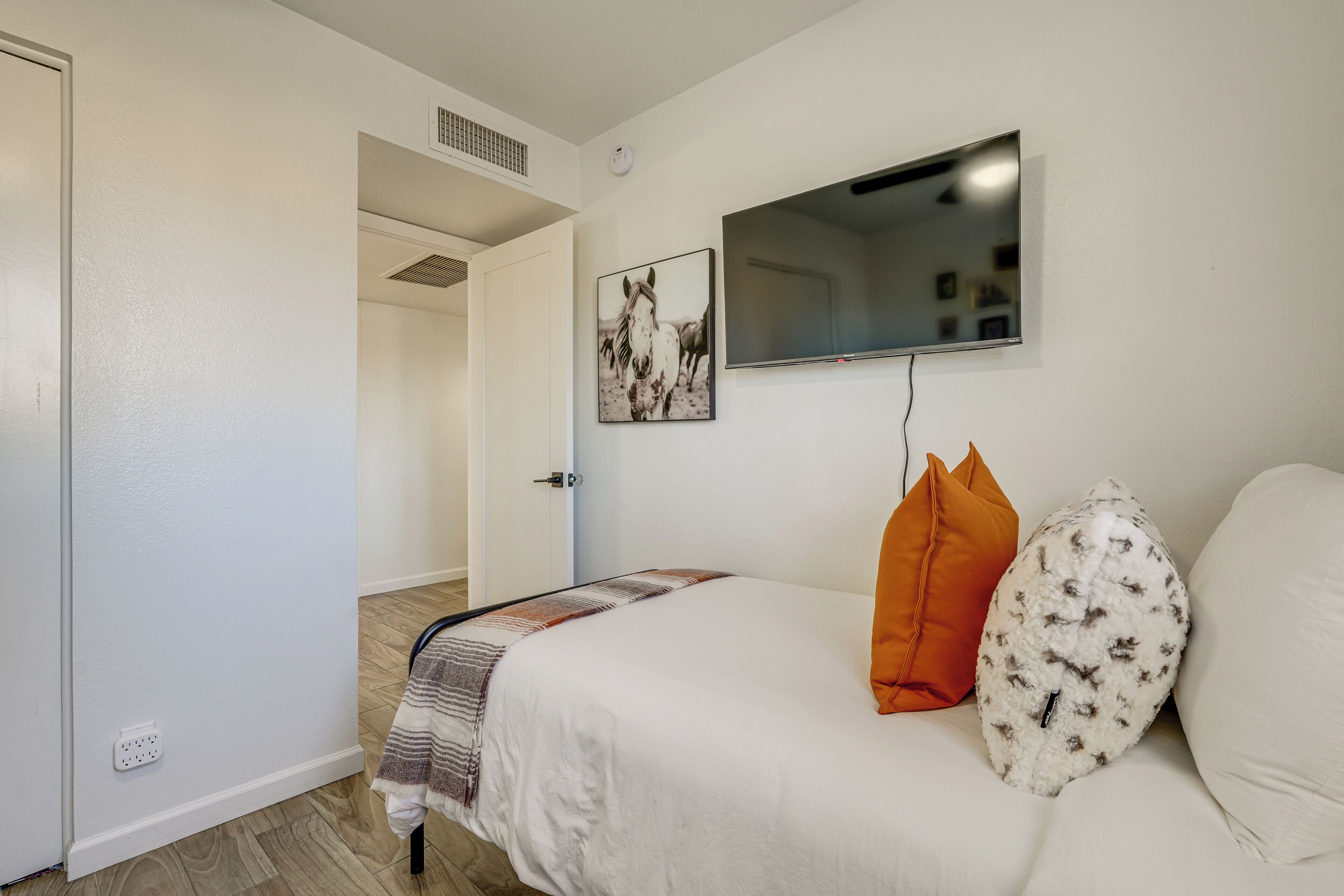 A bedroom with a bed, a TV mounted on the wall, a door, and a window.
