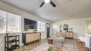 A living room with a wooden floor, a brown leather sofa, a white armchair, a wooden coffee table, and a TV on the wall. - Easy Walk to Dtwn Gilbert, Family-friendly Oasis! (Gilbert)