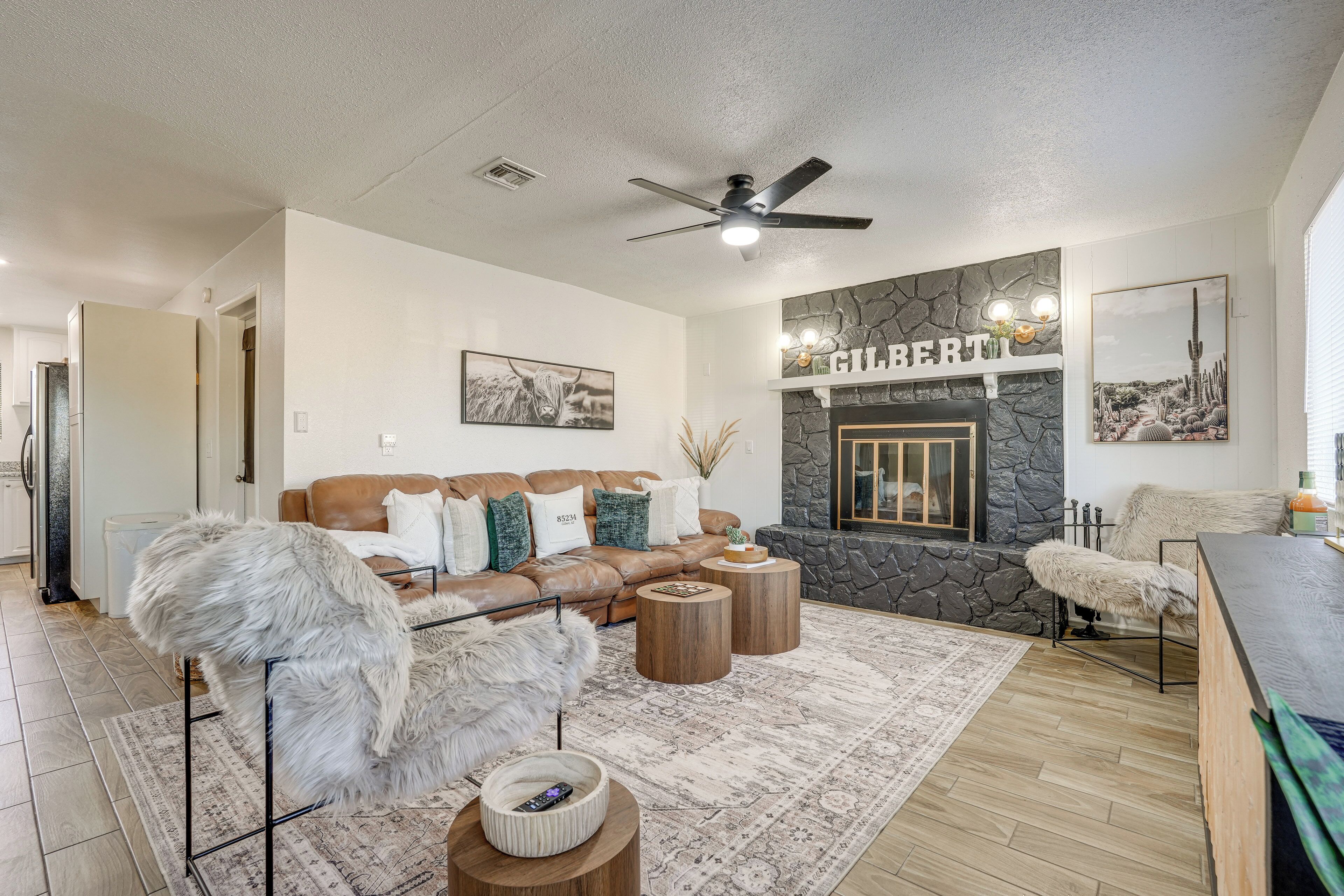 A modern living room with a stone fireplace, a ceiling fan, and a large brown leather sofa.