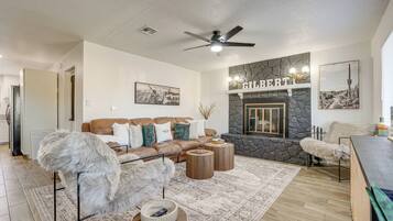 A modern living room with a stone fireplace, a ceiling fan, and a large brown leather sofa.