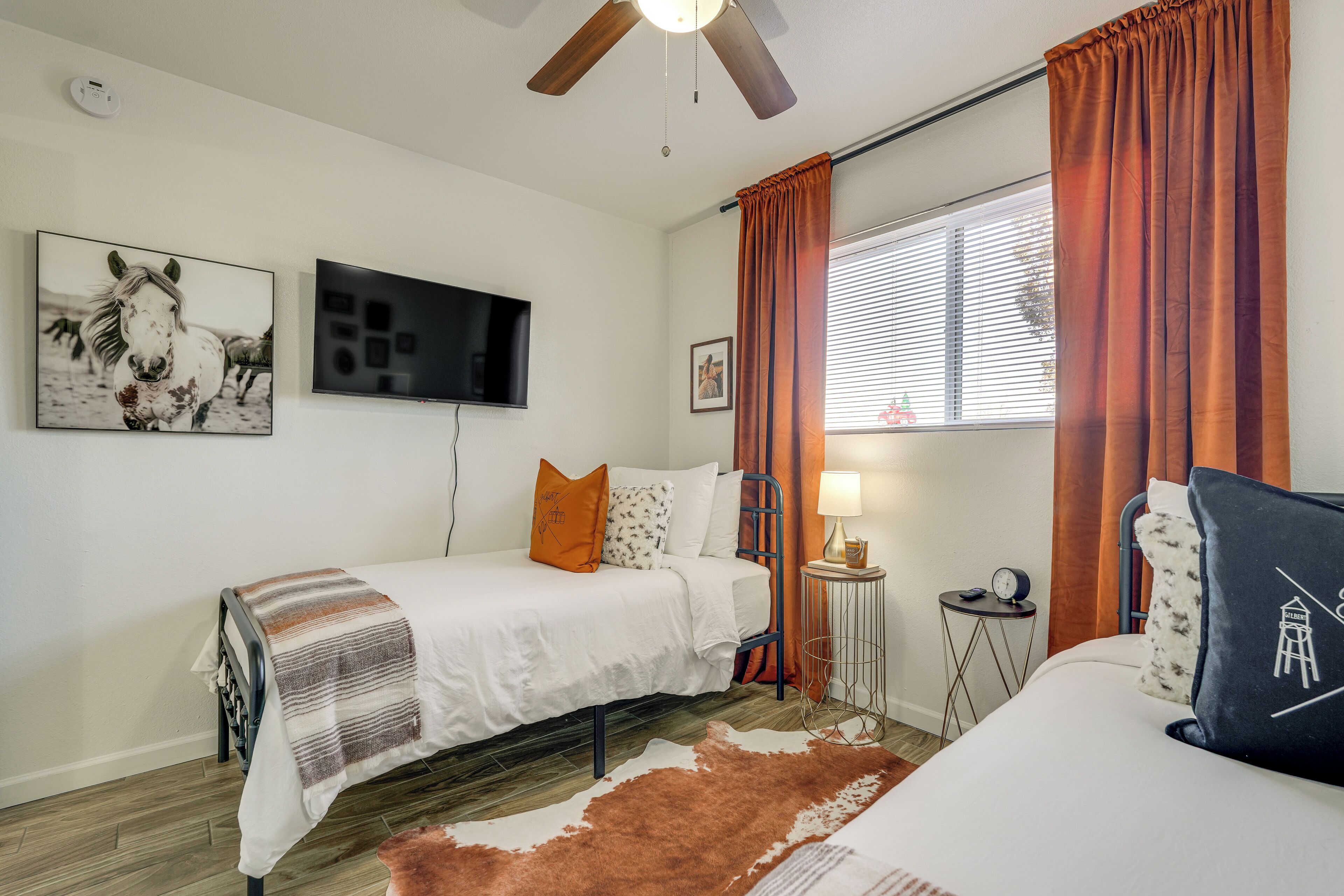 A bedroom with a bed, a TV, a small table with a lamp, and a window with curtains.