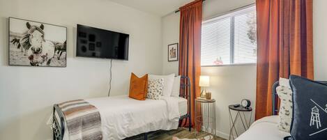 A bedroom with a bed, a TV, a small table with a lamp, and a window with curtains.