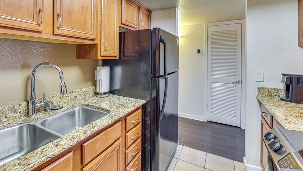 A kitchen with granite countertops, stainless steel sink, wooden cabinets, a black refrigerator, and a microwave. - Quiet & Convenient! Condo w/ Balcony Near ASU (Tempe)
