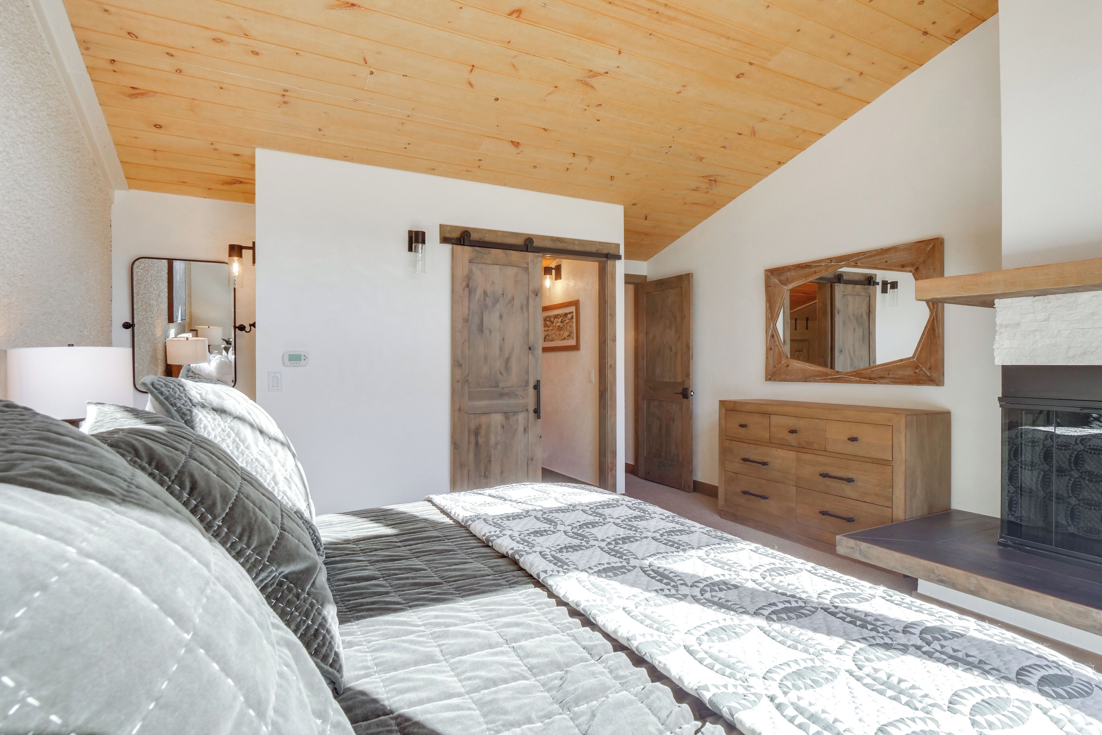 Ein Schlafzimmer mit Holzbalkendecke, einem Bett mit gemusterten Betttextilien, einem Schminktisch, einem Spiegel und einem Kamin.