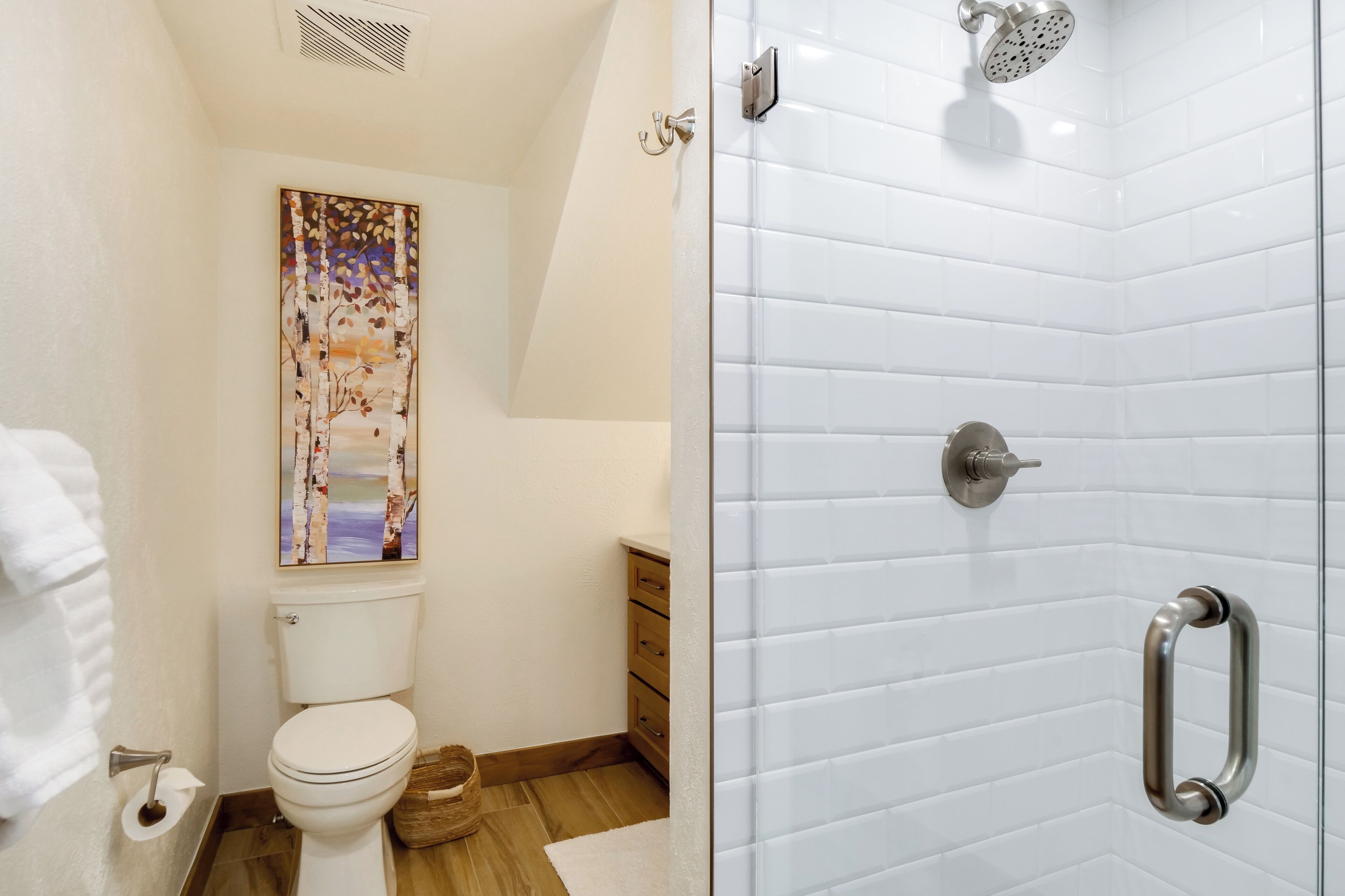 Um banheiro moderno com vaso sanitário, chuveiro com porta de vidro e piso de madeira.