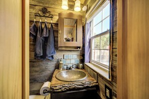 Une salle de bain rustique avec un meuble-lavabo en bois, un grand miroir et une fenêtre laissant entrer la lumière naturelle.