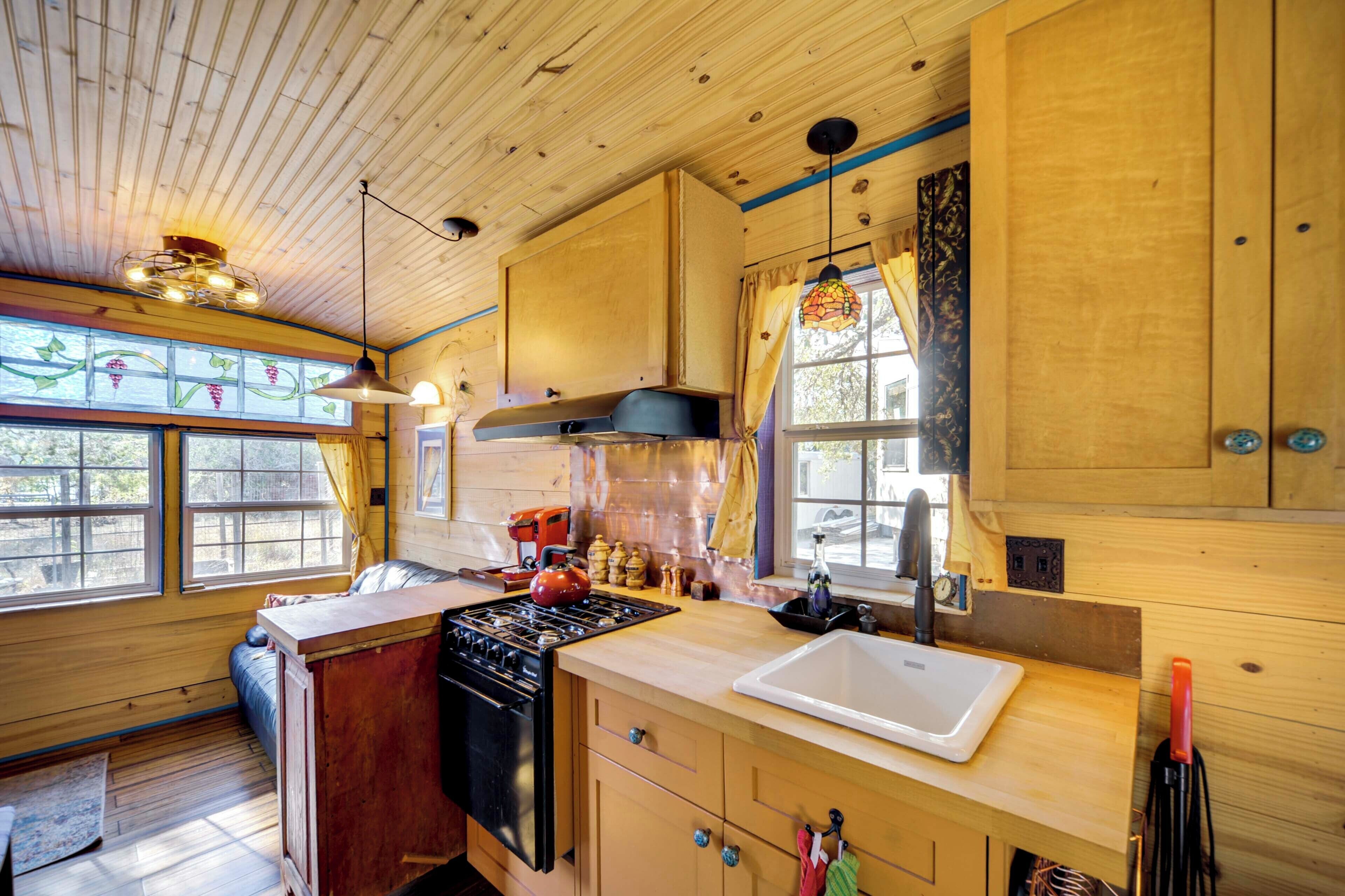 A wooden cabin kitchen with a stove, sink, and cabinets.