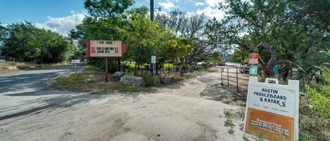 A dirt road leading to a gated area with signs for Austin Paddleboard & Kayak and Live Music events.