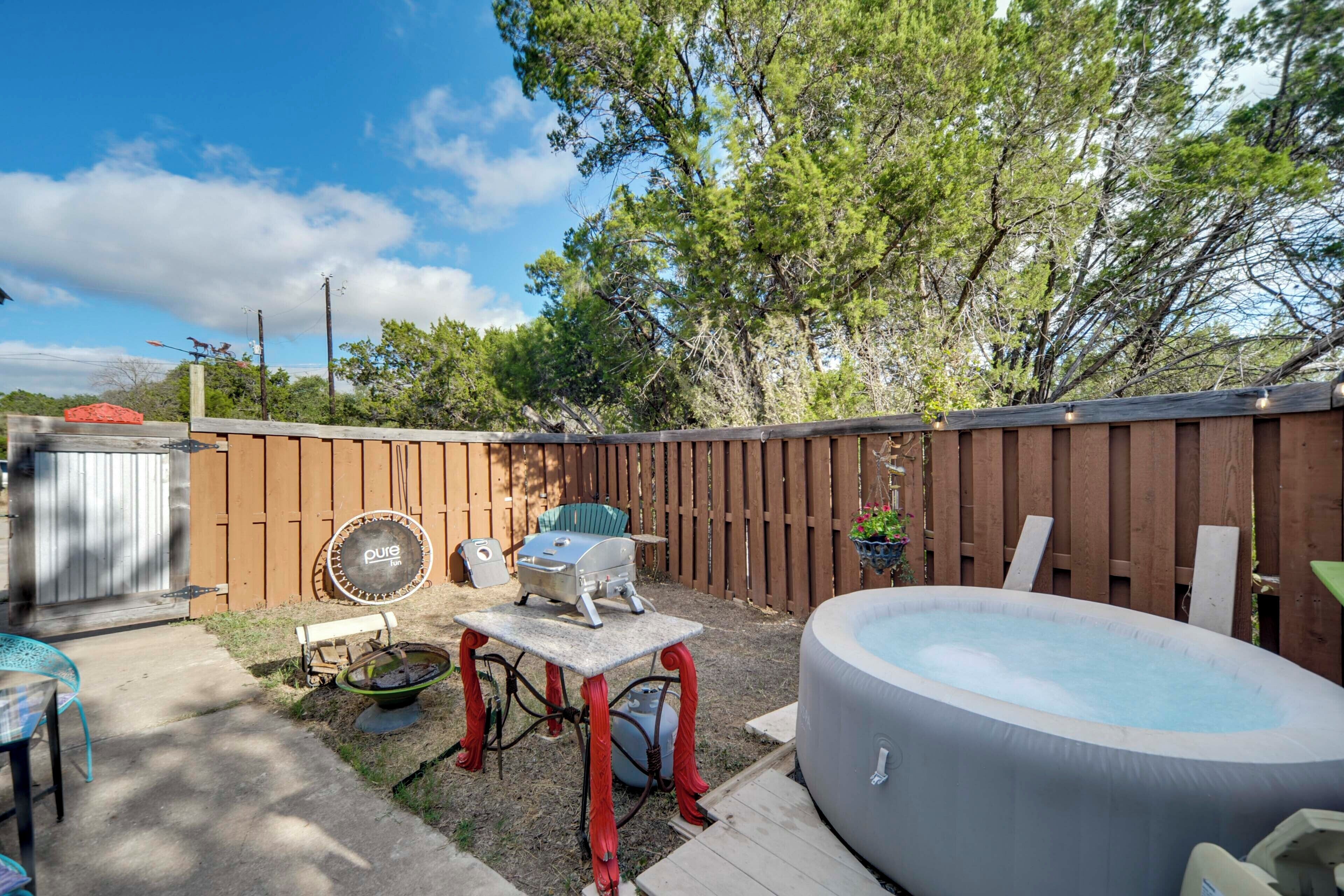 A backyard with a hot tub, a barbecue grill, and a table with chairs.