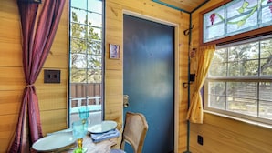 A wooden room with a blue door, a table with a glass top, and a chair. - Walk to Lake Travis: Austin Tiny Home w/ Hot Tub! (Lakeway)