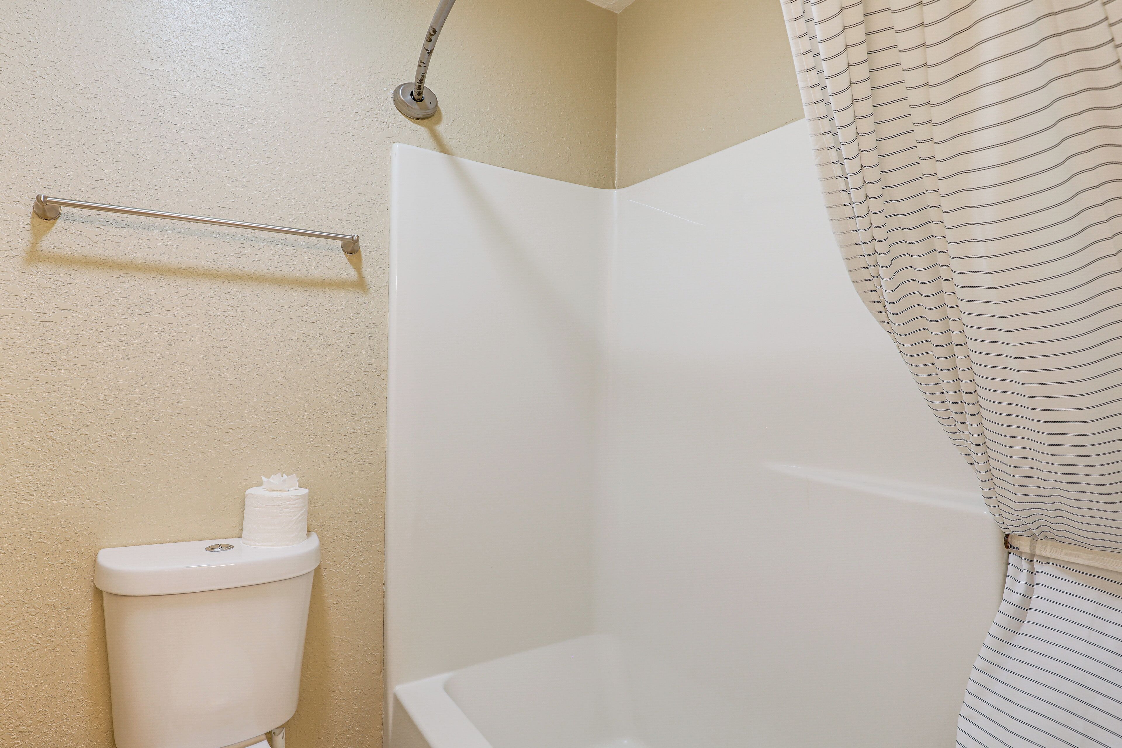 A bathroom with a toilet, a shower with a striped curtain, and a towel rack.