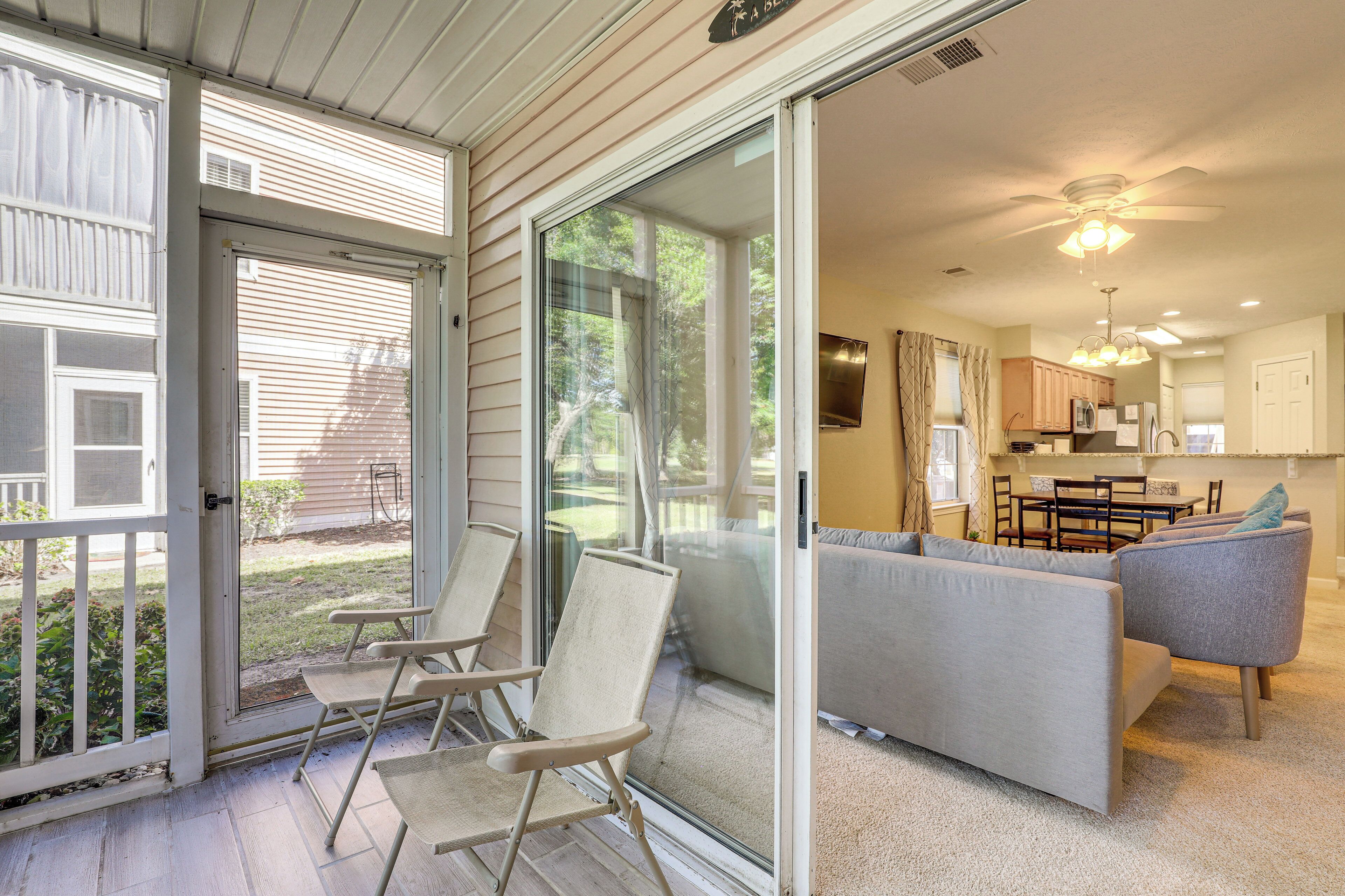 A spacious living area with a sliding glass door leading to a patio, a gray sofa, and a dining area with a table and chairs.