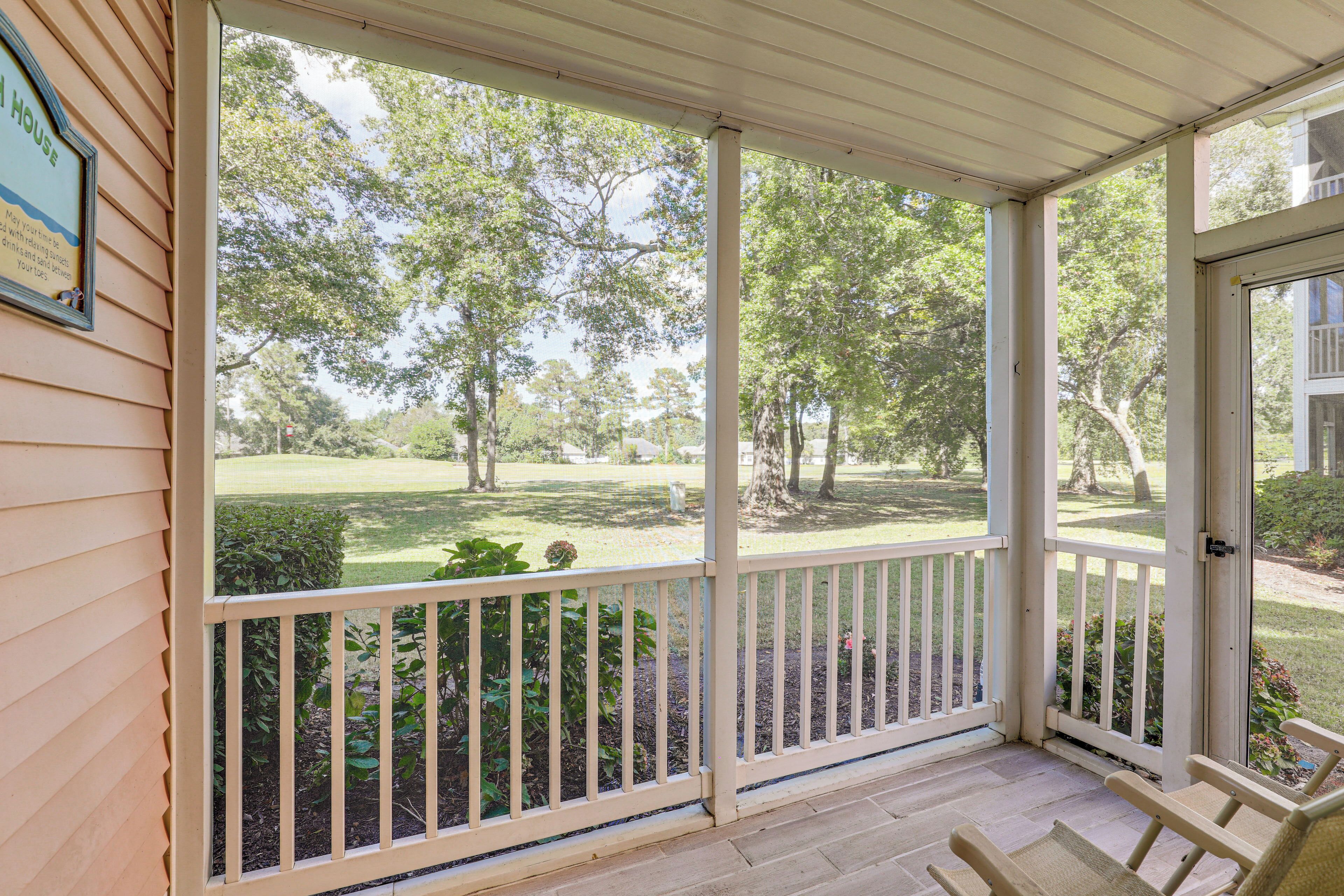 A covered porch with a view of a grassy yard and trees.