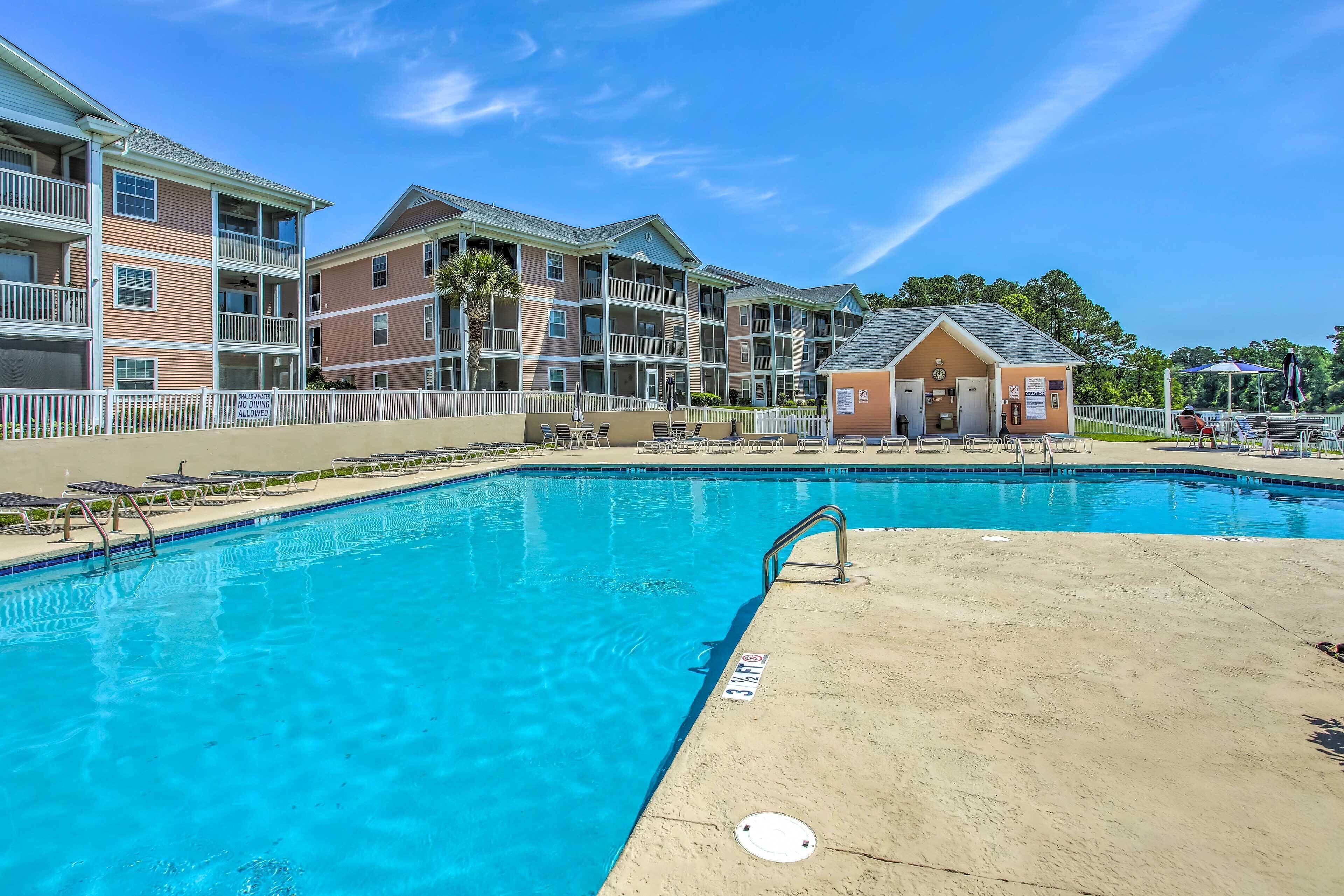 A swimming pool with a lifeguard stand, a small building, and a fenced area with lounge chairs.