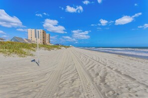 A sandy beach with footprints leading to a building with multiple floors.