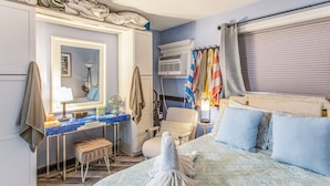 A hotel room with a bed, a desk, a chair, a vanity with a mirror, and an air conditioning unit. - Steps to Shore + Pier: Condo in North Myrtle Beach (North Myrtle Beach)