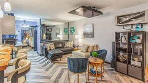 A modern living room with a sofa, armchairs, a coffee table, and a bookshelf. - Steps to Shore + Pier: Condo in North Myrtle Beach (North Myrtle Beach)