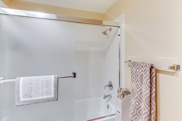 A bathroom with a glass shower enclosure, a white bathtub, and a towel rack with a patterned towel. - Golf Course View & Pool Access: Palm Desert Condo (Palm Desert)