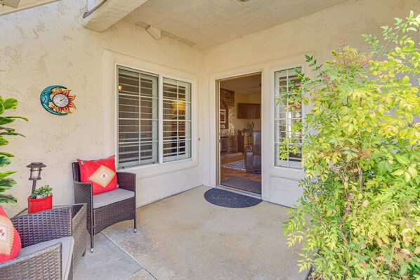 A covered patio area with wicker furniture, a potted plant, and a decorative wall clock. - Golf Course View & Pool Access: Palm Desert Condo (Palm Desert)