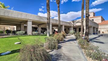 A building with a covered outdoor area, palm trees, and a well-maintained lawn.