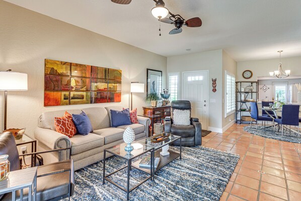 A spacious living room with a sofa, coffee table, and a dining area with chairs and a chandelier. - Golf Course View & Pool Access: Palm Desert Condo (Palm Desert)