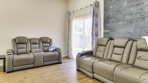 Ein Wohnzimmer mit zwei beigefarbenen Ledersofas, Holzboden, Steinwand und einem Fenster mit transparenten Vorhängen.