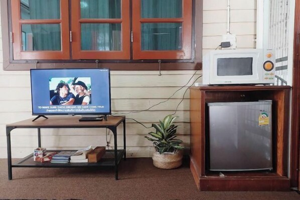 A room with a television on a stand, a small refrigerator, and a window with curtains. - The Warehouse - Ayutthaya (Ayutthaya)