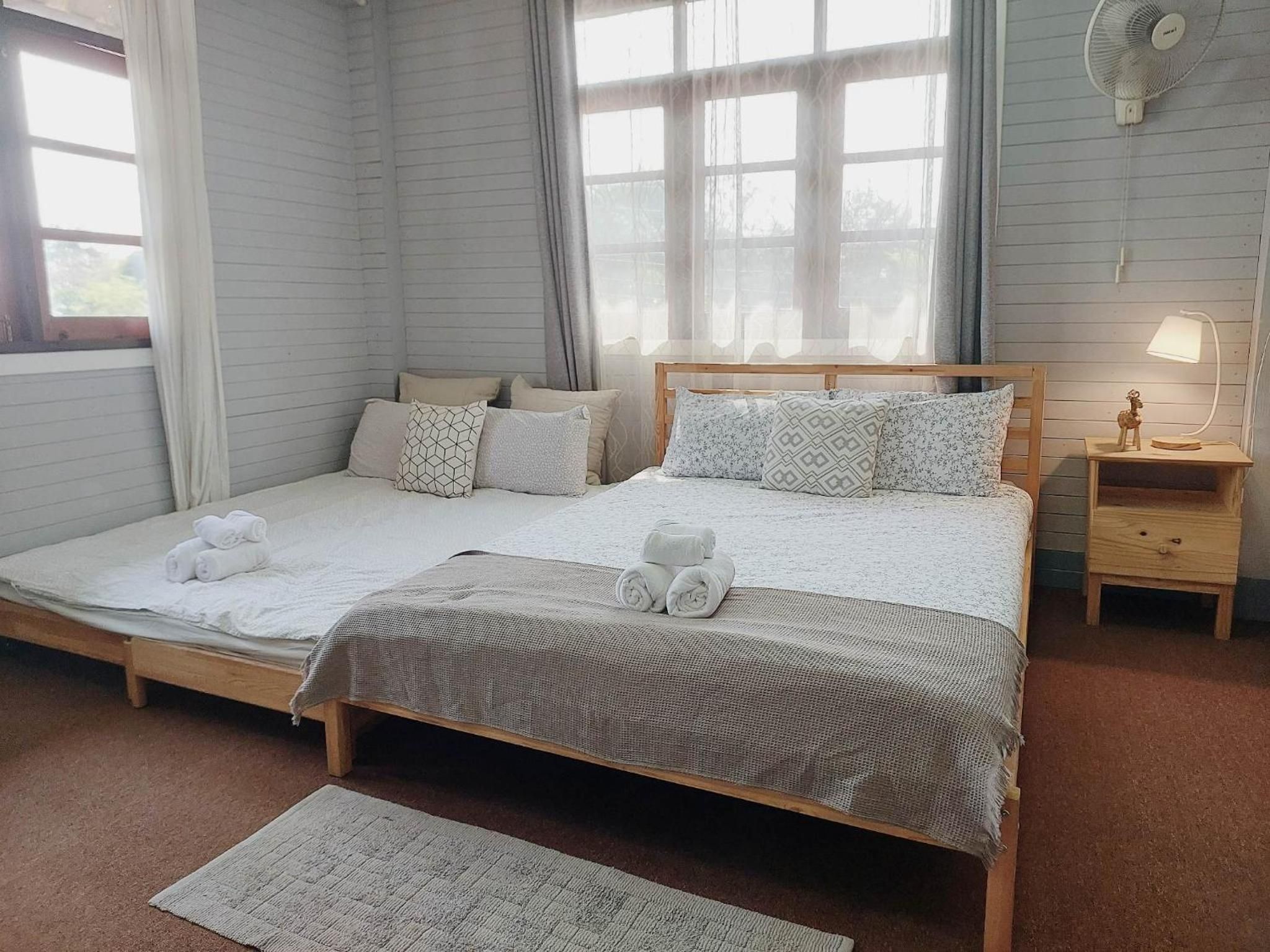 Een tweepersoonsbed met houten frame, twee nachtkastjes, een raam met gordijnen.